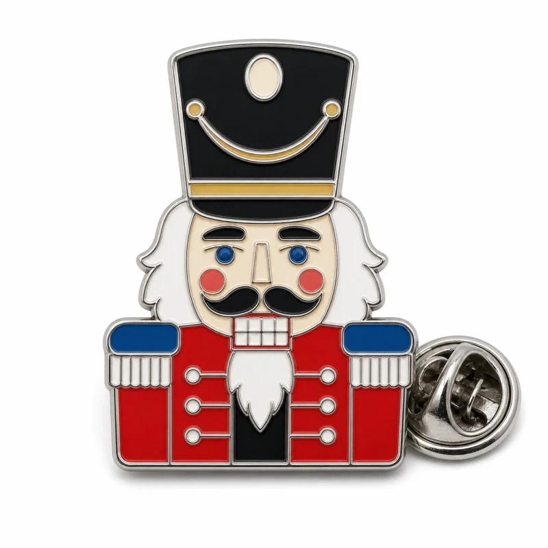 Pin de cascanueces de tambor mayor con contornos de metal plateado pulido, sombrero negro alto, chaqueta roja, barba blanca, paneles azules y un embrague de mariposa sobre blanco.