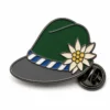 Spilla per cappello bavarese Edelweiss con contorni in nichel nero, cappello verde scuro, tesa grigia, fiore di stella alpina color crema e frizione a farfalla su sfondo bianco.