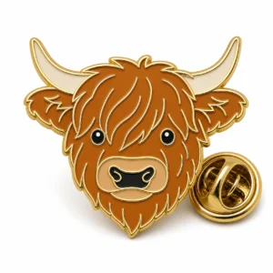 Fluffy face Highland cow pin with raised gold metal outlines, shaggy brown hair, cream horns, tan muzzle, and a butterfly clutch on white.