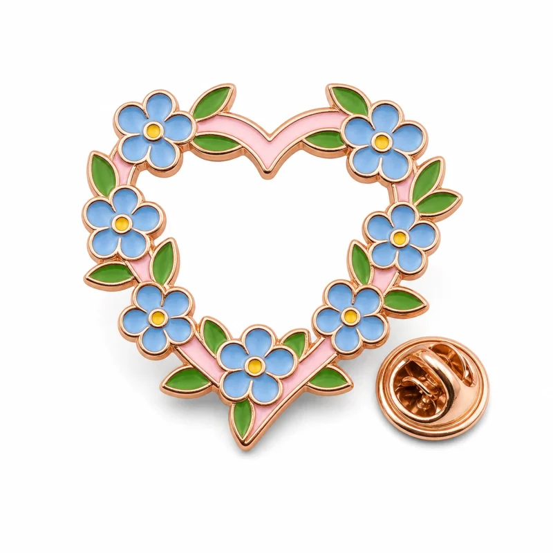 Epingle "forget me not" en forme de couronne de coeur avec des contours en métal doré rose, des fleurs émaillées bleues, des feuilles connectées vertes, un cadre en forme de coeur rose et une pochette en forme de papillon sur fond blanc.