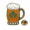 Épingle en émail souple représentant un récipient à bière en forme de houblon et d'orge, avec émail ambré, motif de houblon vert, lignes métalliques en relief, couvercle en mousse et pochette de papillon sur fond blanc.