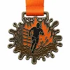 Медаль с мягкой эмалью Mud splash Tough Mudder Medal с металлическими контурами цвета античной бронзы, оранжевой лентой, силуэтом бегуна, грязевой тропой, фигурами брызг, полосами препятствий и белым фоном.