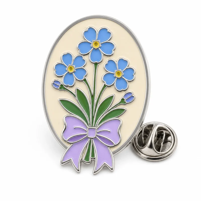 Broche bouquet ovale forget me not avec contours en métal argenté, base ovale crème, fleurs bleues, tiges vertes, nœud lavande et pochette papillon sur fond blanc.