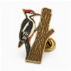 Perched Woodpecker Pin aus weicher Emaille mit erhabenen Metallkonturen, flachen Emaille-Farbabschnitten, verbundenen Abzeichendetails und einem Schmetterlingsgriff auf weißem Hintergrund.