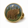 Épingle ronde en forme d'ours brun de la forêt Épingle en émail mou avec des contours métalliques en relief, des sections plates en émail, des détails de badge connectés et une pochette de papillon sur un fond blanc.