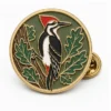 Runder Woodland Woodpecker Pin aus weicher Emaille mit erhabenen Metallkonturen, flachen Emaille-Farbabschnitten, verbundenen Abzeichendetails und einem Schmetterlingsgriff auf weißem Hintergrund.