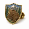Épingle de l'ours brun en bouclier Épingle en émail mou avec des contours métalliques en relief, des sections d'émail plat, des détails de badge connectés et une pochette de papillon sur un fond blanc.