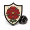 Shield English Rose Pin Anstecknadel aus weicher Emaille mit erhabenen Metallkonturen, flachen Emaille-Farbabschnitten, verbundenen Abzeichendetails und einem Schmetterlingsgriff auf weißem Hintergrund.