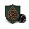 Shield Pine Cone Pin soft enamel pin with raised metal outlines, flat enamel color sections, connected badge details, and a butterfly clutch on a white background.