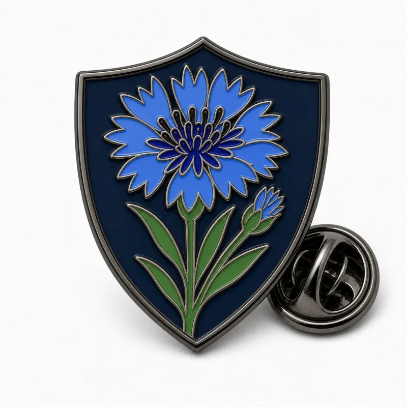 Spilla a forma di rametto di fiordaliso con contorni in nichel nero, base dello scudo in marina profonda, fiordaliso blu, gambo e foglie verdi e frizione a farfalla su sfondo bianco.