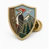 Shield Woodpecker Pin Anstecknadel aus weicher Emaille mit erhabenen Metallkonturen, flachen Emaille-Farbabschnitten, verbundenen Abzeichendetails und einem Schmetterlingsgriff auf weißem Hintergrund.