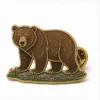 Épingle en forme d'ours brun debout épingle en émail mou avec des contours métalliques en relief, des sections de couleur émaillée plate, des détails de badge connectés et une pochette de papillon sur fond blanc.