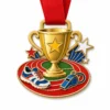 Медаль "День спорта" из мягкой эмали с контурами из полированного золотистого металла, красной лентой на шее, формой кубка, дорожками для бега, акцентами в виде звезды, свистка и кроссовок и белым фоном.