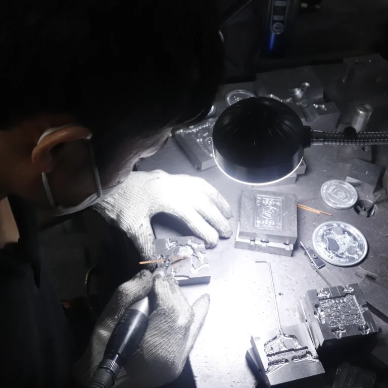 A worker carefully opening the sprue of a metal mold, allowing molten zinc alloy to flow into the mold cavities, with gloves and flashlight for precision.