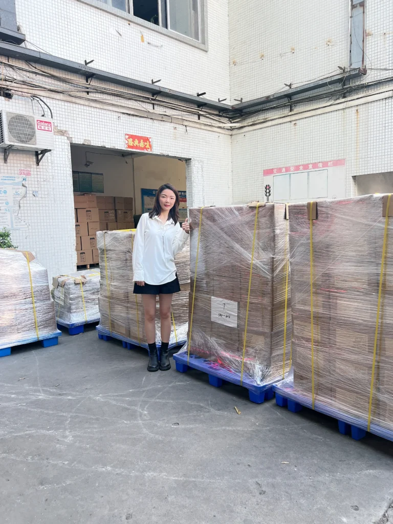 A warehouse worker standing beside large pallets of products wrapped with protective stretch film and secured with straps, demonstrating strong and durable packaging for safe transportation.