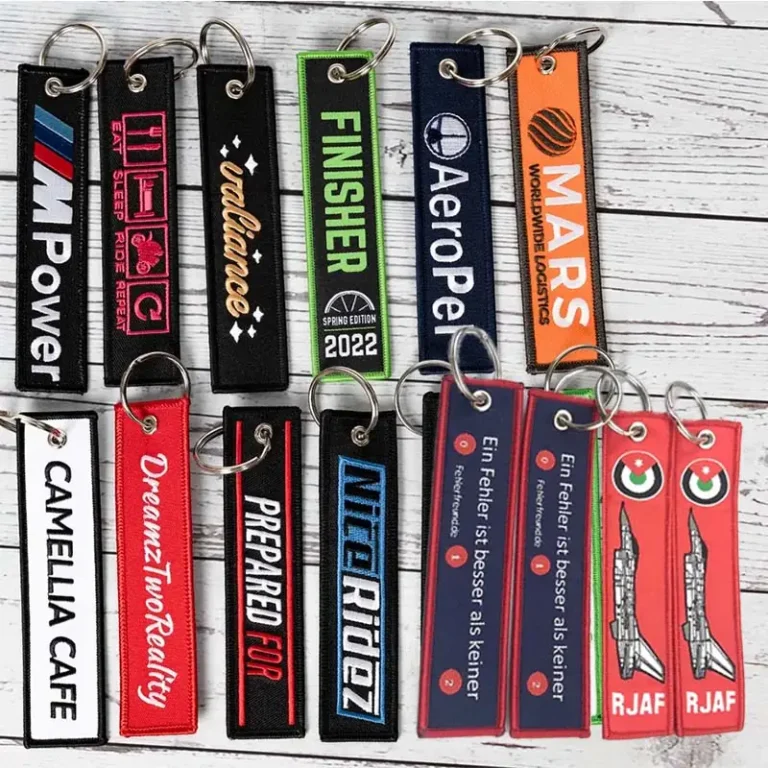 A collection of custom embroidered jet tag keychains with metal rings, featuring aviation, motorcycle, racing, logistics, finisher, and branded text designs in multiple colors.
