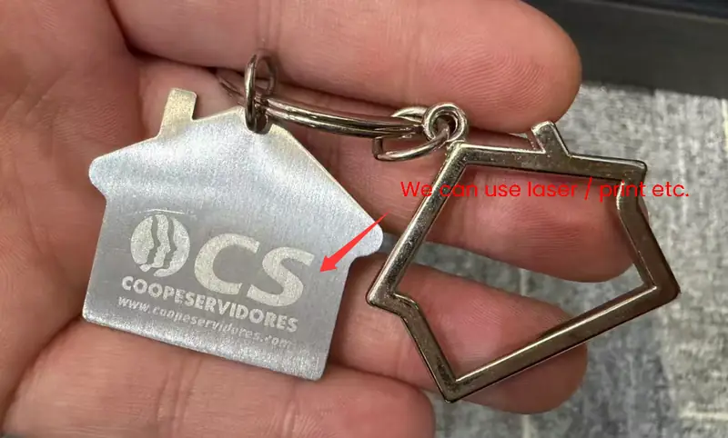 A custom silver-tone house-shaped metal keychain featuring a laser engraved DCS COOPESERVIDORES logo and website, paired with an open-frame house charm and metal key ring.
