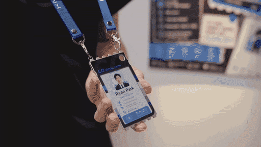 An animated GIF showing a person holding a digital business card badge with a color display, employee photo, name, contact details, and blue lanyard at a professional event.